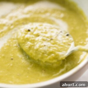 Velvet Asparagus Soup 11 A comforting cream of asparagus soup garnished with cracked black pepper served in a white bowl with a silver metal spoon.