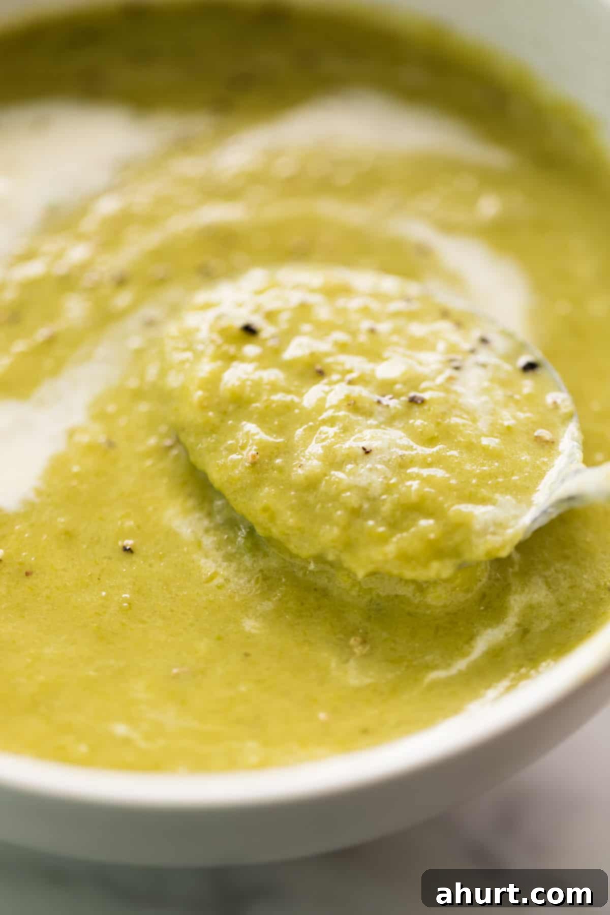 Velvet Asparagus Soup 10 A comforting white bowl of cream of asparagus soup garnished with cracked black pepper. Served with a silver metal spoon in the soup ready to enjoy