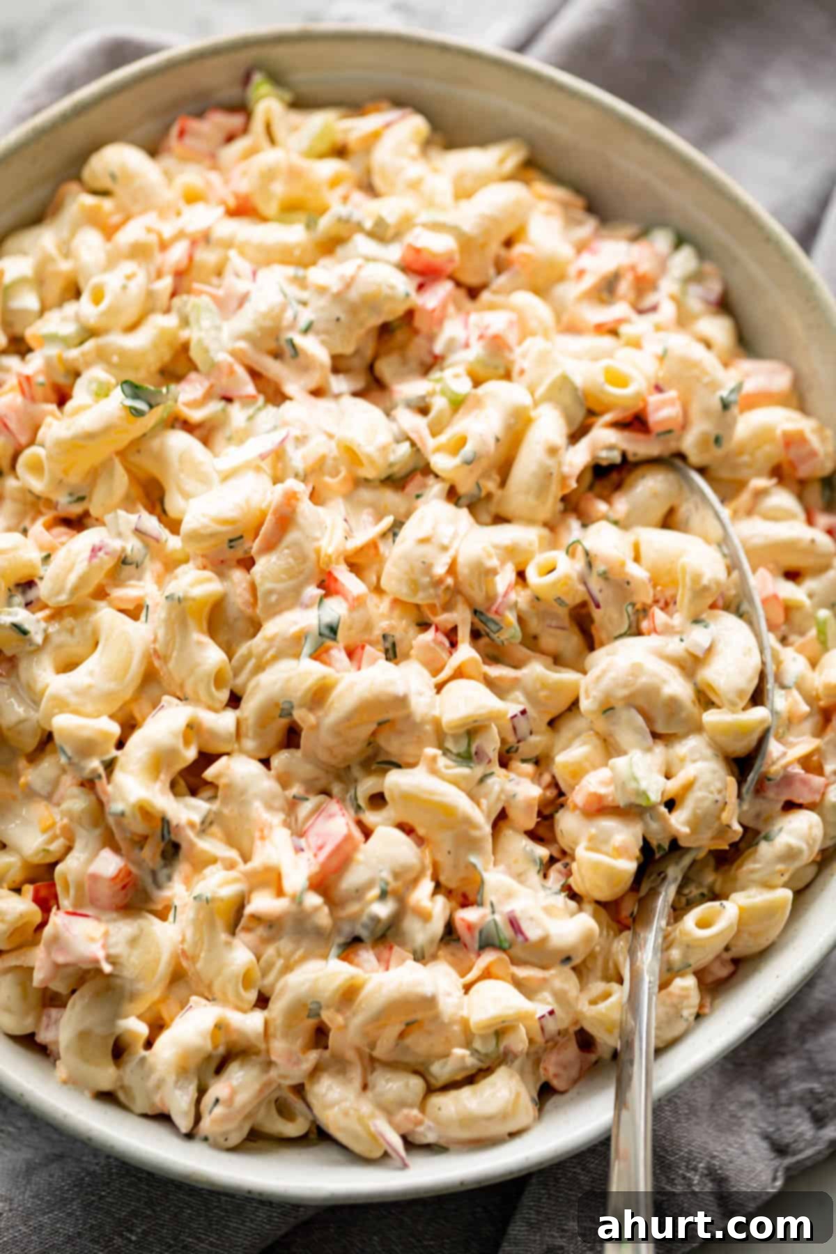Picnic Perfect Macaroni Salad 2 Delicious Macaroni Salad, quick to prepare and served in a light grey bowl on a grey linen cloth with a spoon for scooping.
