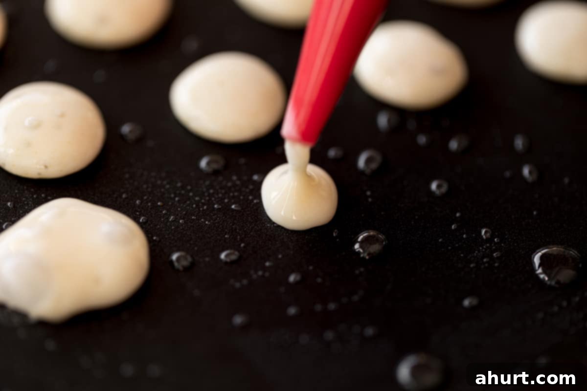 Piping batter into small circles using a squeeze bottle onto a nonstick pan lightly greased with oil.