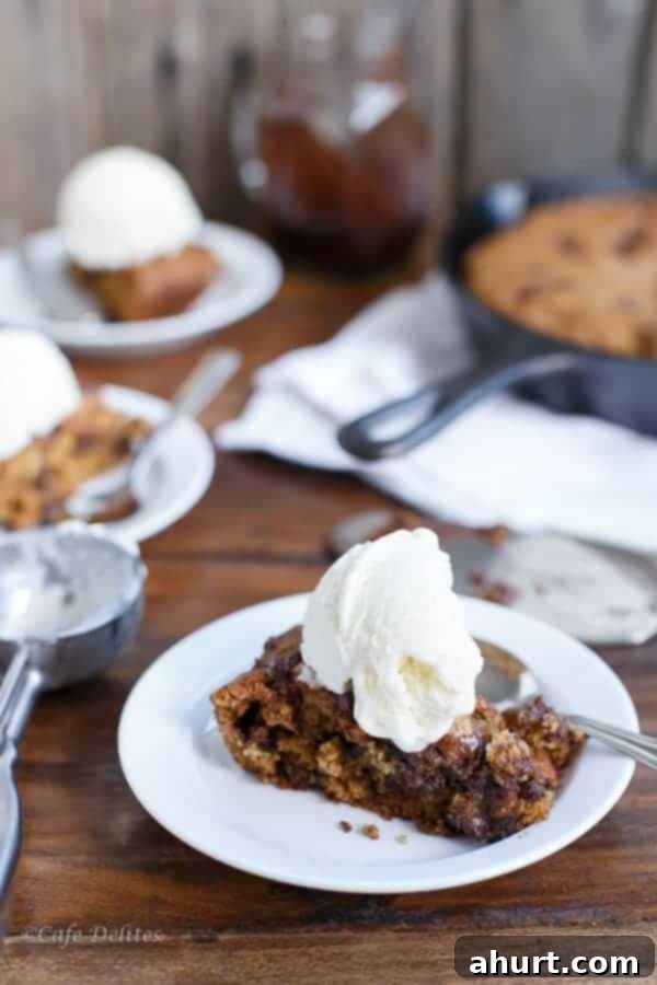 A slice of Peanut Butter Chocolate Chip Deep Dish Skillet Cookie on a plate, topped with a scoop of vanilla ice cream.