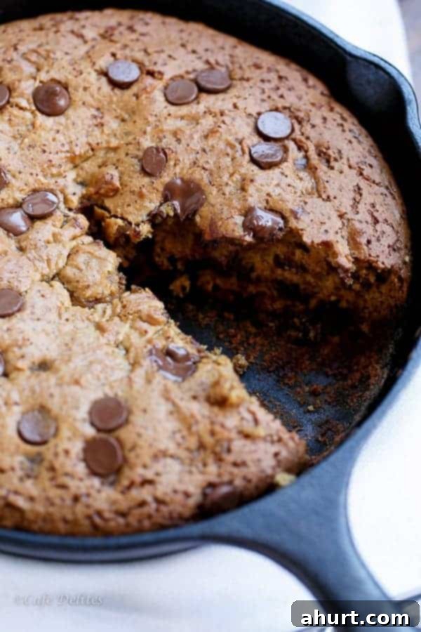 A freshly baked Peanut Butter Chocolate Chip Deep Dish Skillet Cookie with a missing slice, revealing its warm, soft interior.