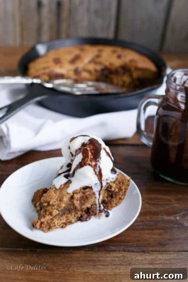 A slice of Peanut Butter Chocolate Chip Deep Dish Skillet Cookie on a white plate, topped with a scoop of ice cream, showing the cookie's thickness and rich toppings.