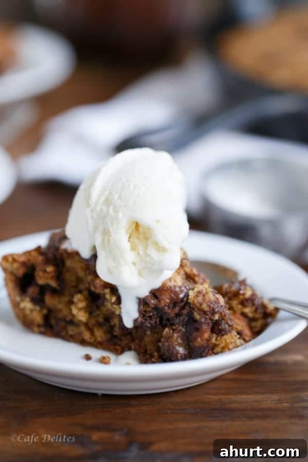 A close-up of a serving of Peanut Butter Chocolate Chip Deep Dish Skillet Cookie, topped with a generous scoop of ice cream, highlighting the dessert's creamy and warm contrast.