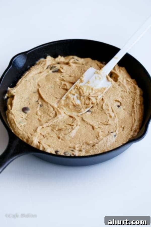 Cookie dough being scooped into a cast iron skillet, ready for baking.