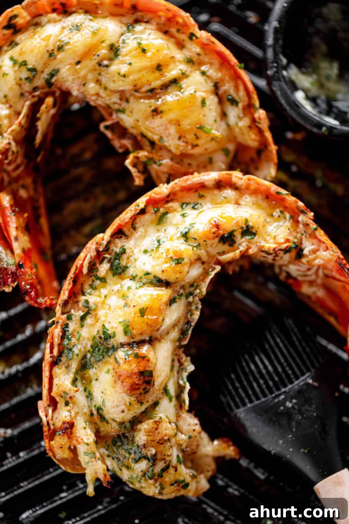 Perfect Grilled Lobster Tails 2 Grilled Lobster Tails garnished with melted garlic herb butter on a black grill pan.