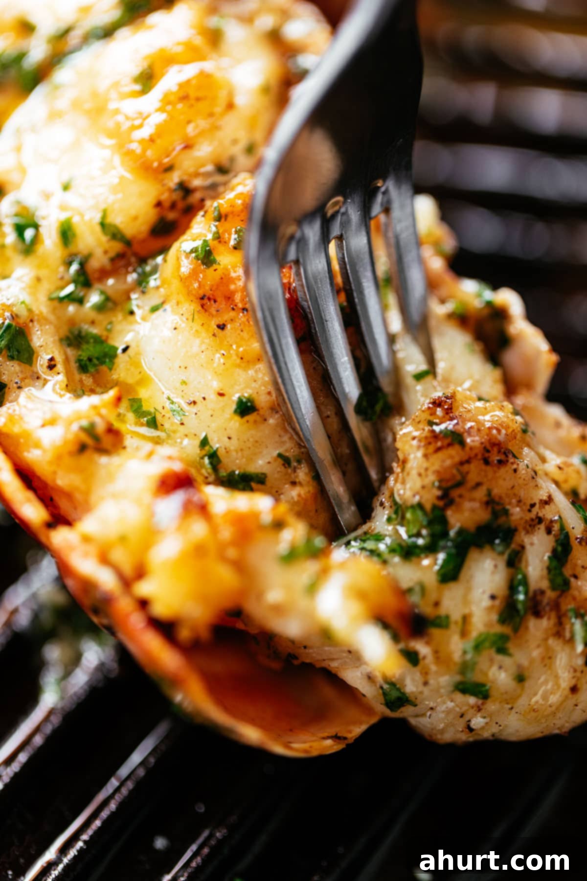 Perfect Grilled Lobster Tails 3 A fork pierces through a grilled lobster tail brushed with melted garlic herb butter on a black grill pan.