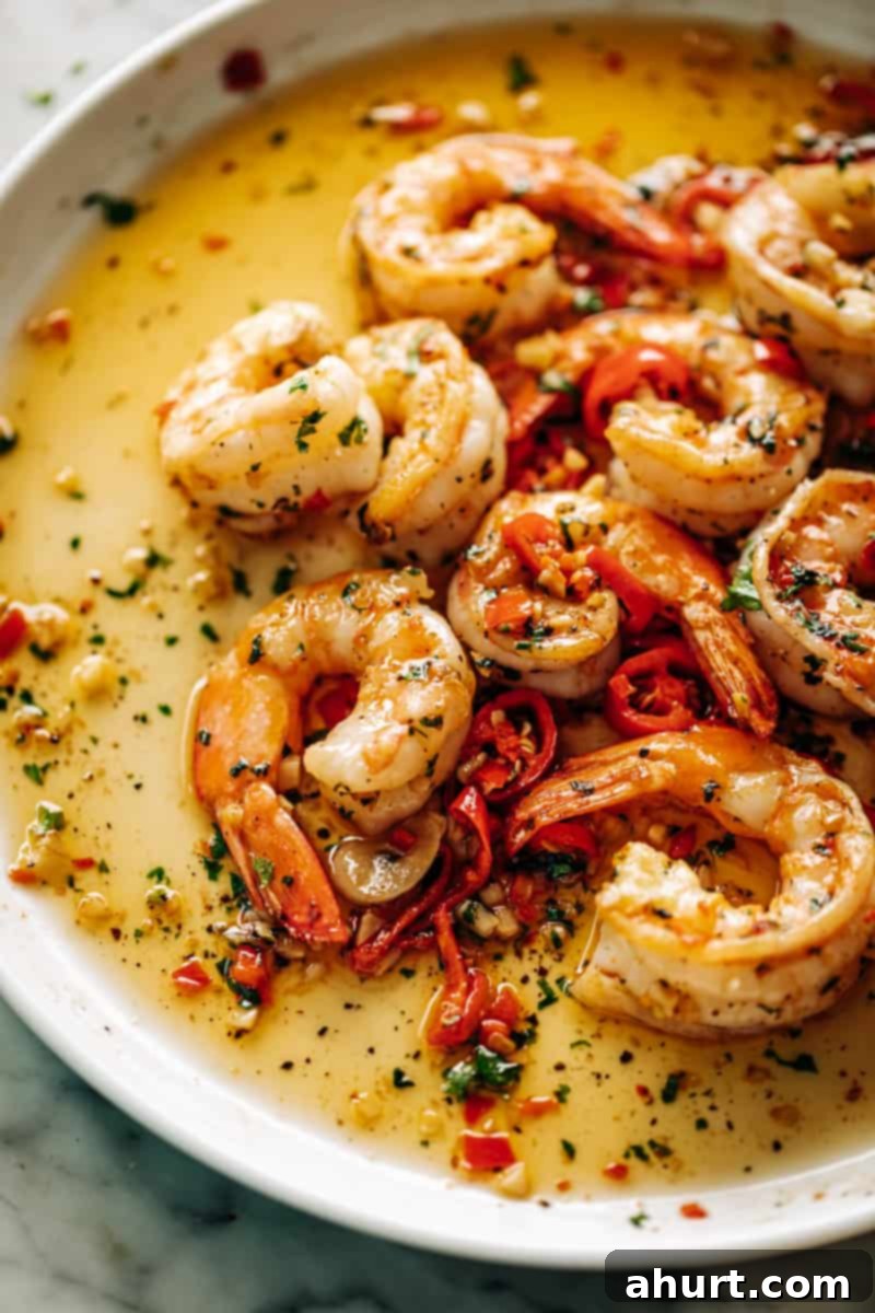Perfect Garlic Butter Shrimp 8 A close-up of a perfectly cooked serving of Chili Garlic Butter Shrimp on a white plate, glistening with a rich sauce, adorned with vibrant red chili pieces and fresh green parsley.