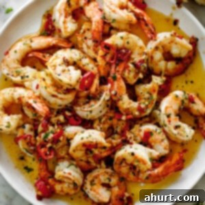 Perfect Garlic Butter Shrimp 9 A pile of shrimp on a white plate sitting in chili garlic butter sauce. Served with broken bread pieces.