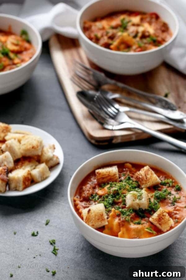 A close-up of a serving of One Pot Creamy Tomato Beef Ravioli in a bowl, garnished with fresh parsley, with a fork and spoon ready to dive in. The rich, creamy sauce coats the tender ravioli, hinting at the delicious flavors within.