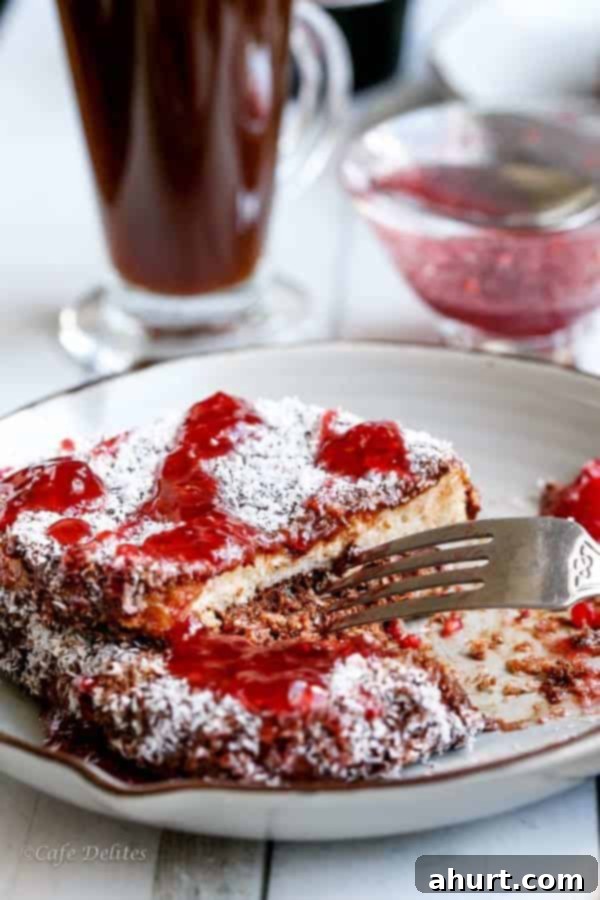 Lamington French Toast with Sweet Raspberry Drizzle 4 Fork piercing into a piece of Lamington French Toast with Raspberry Jam Syrup, showing the fluffy interior and decadent coating