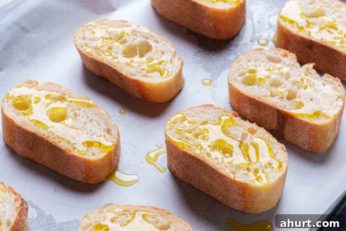 Zesty Caprese Crostini with Smoky Grilled Avocado 5 crostinis arranged on a baking sheet drizzled with olive oil are ready to be place in the oven.
