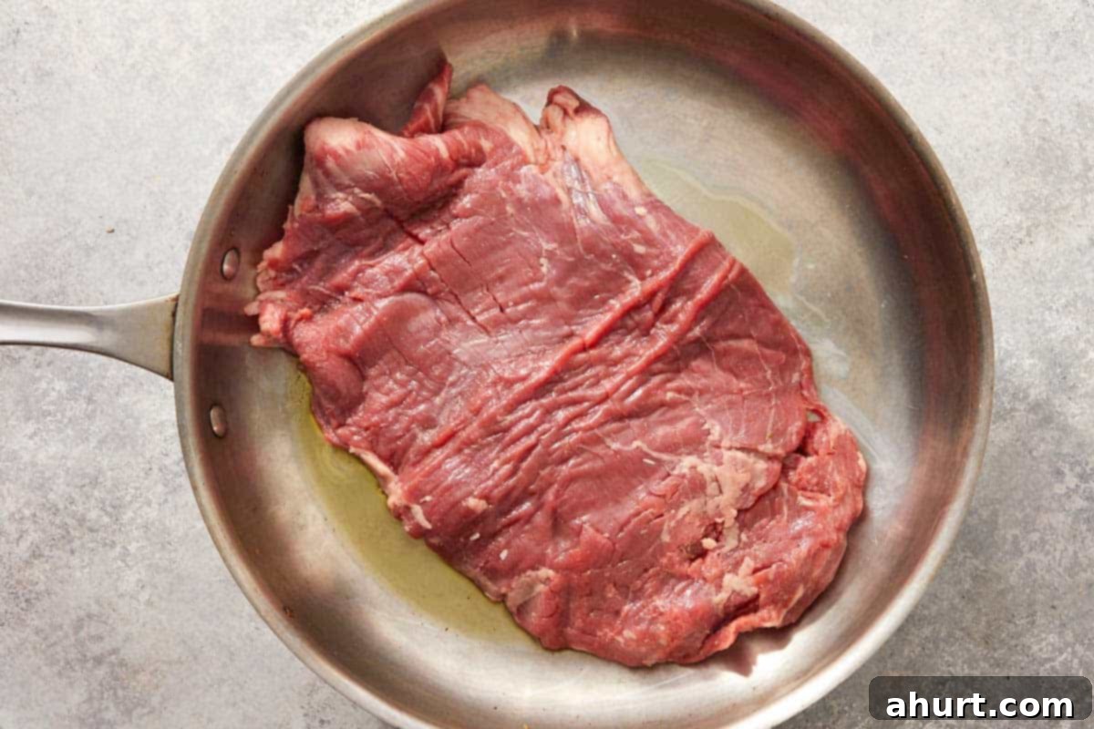 Birria Tacos Simplified 6 Raw flank steak searing in a stainless steel pan.