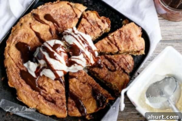 Nutella Stuffed Churro Deep Dish Skillet Cookie being cut into pieces with ice cream scoop and sauce