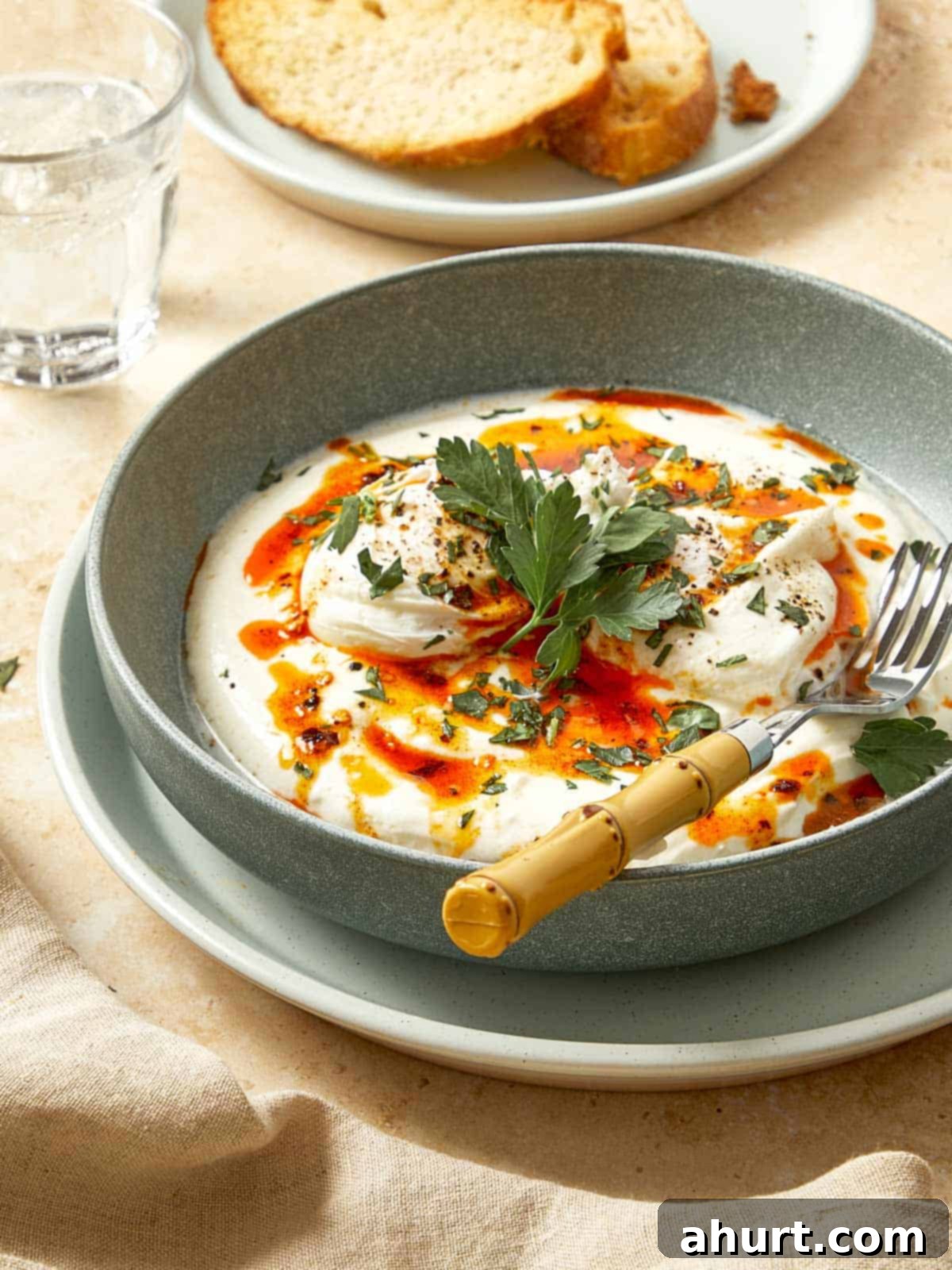 Cilbir Turkish Eggs 10 Turkish eggs served in a bowl with yogurt, poached eggs, chili butter, and fresh herbs, with toasted bread on the side.