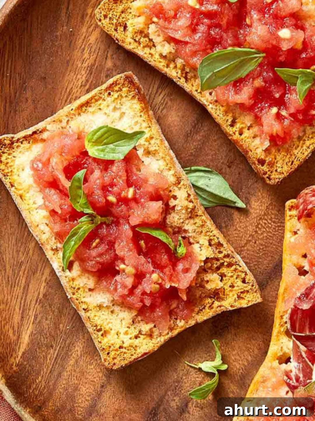 Spanish Tomato Pan Coca 2 Overhead view of Spanish Pan Coca with tomato, basil, and cured ham on toasted bread, styled on a wooden board.