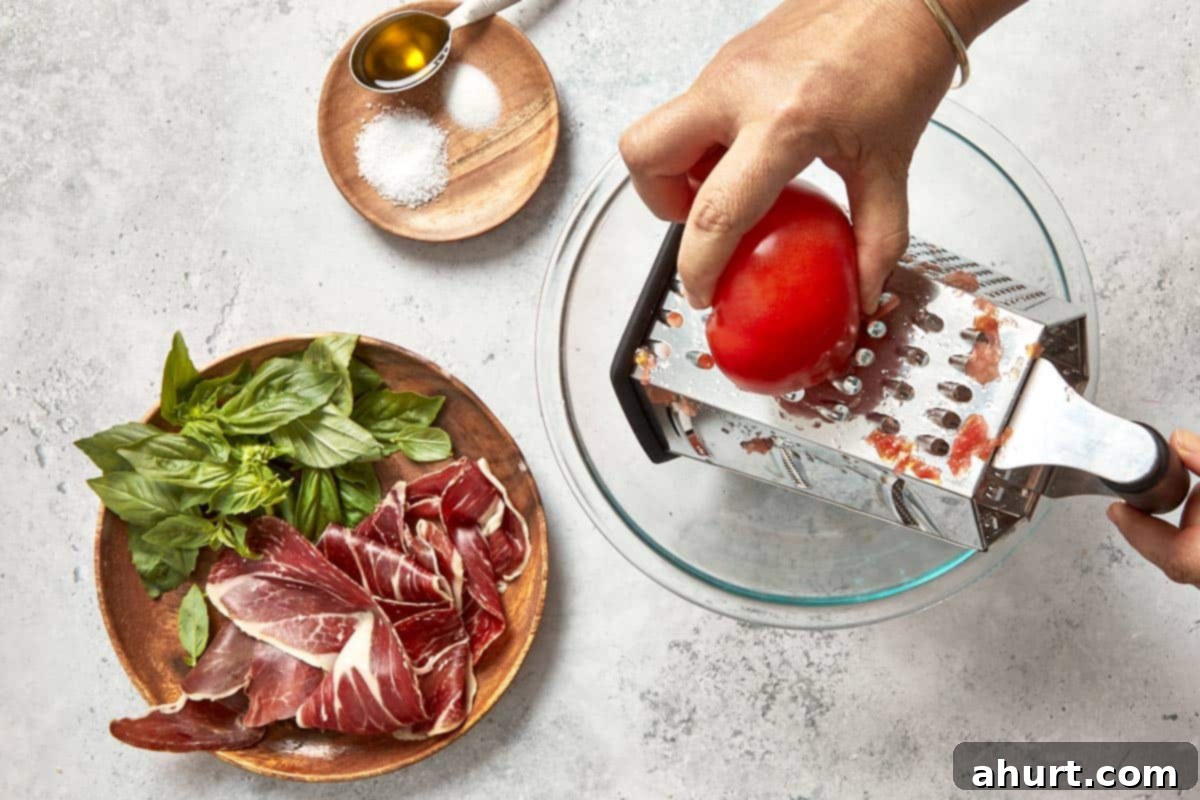 Spanish Tomato Pan Coca 12 Grating a tomato into a bowl beside basil, Jamón Ibérico, and seasoning ingredients.