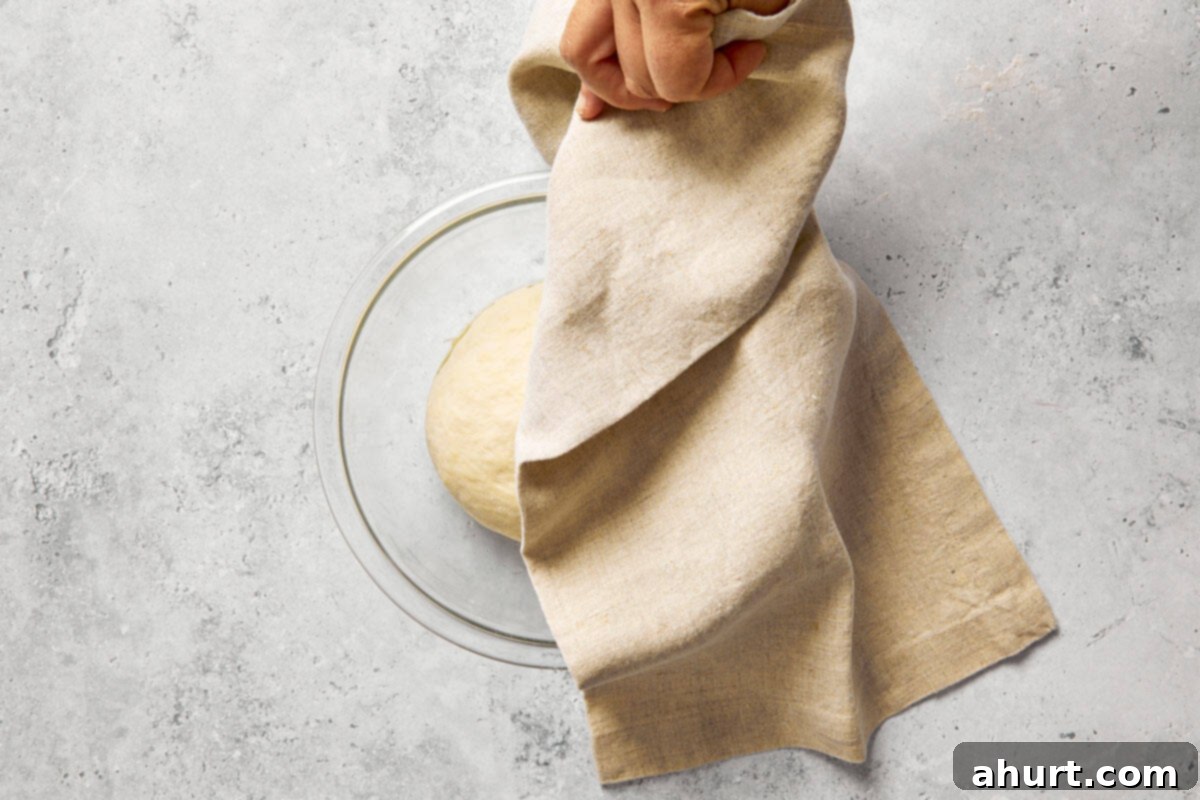 Spanish Tomato Pan Coca 7 Dough covered with a kitchen towel, rising in an oiled glass bowl.