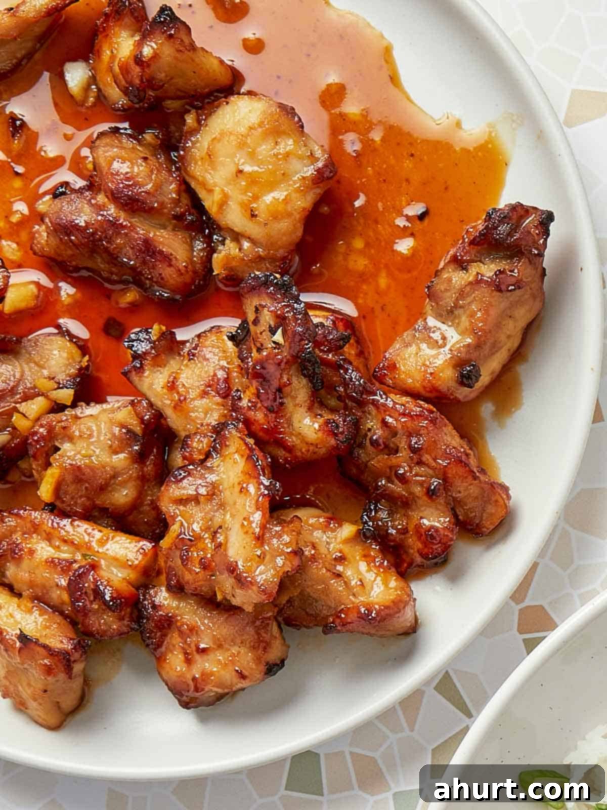 Crispy Air Fryer Teriyaki Chicken Thighs 10 Close-up of crispy air fryer teriyaki chicken glazed with a glossy, garlicky sauce on a white plate