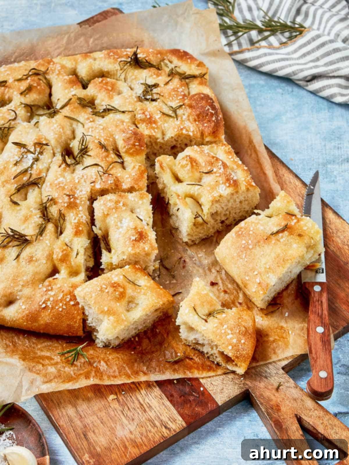 Effortless Homemade Focaccia 2 Baked focaccia bread sliced into squares, topped with sea salt and rosemary, served on parchment paper.