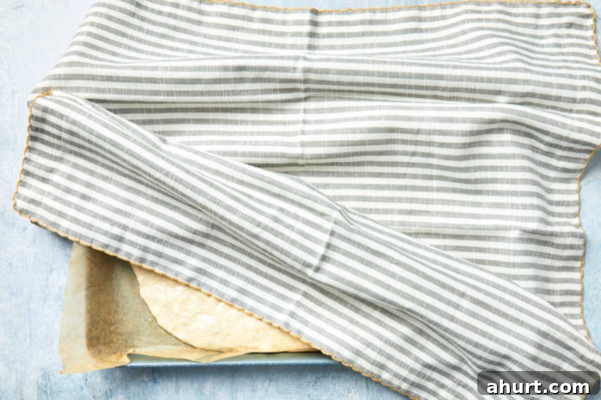 Effortless Homemade Focaccia 11 Baking pan covered with a striped cloth for the first rise, showing the dough's initial expansion.