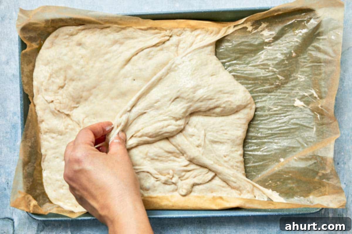 Effortless Homemade Focaccia 12 Dough being gently folded from the sides after rising, demonstrating the stretch and fold technique.