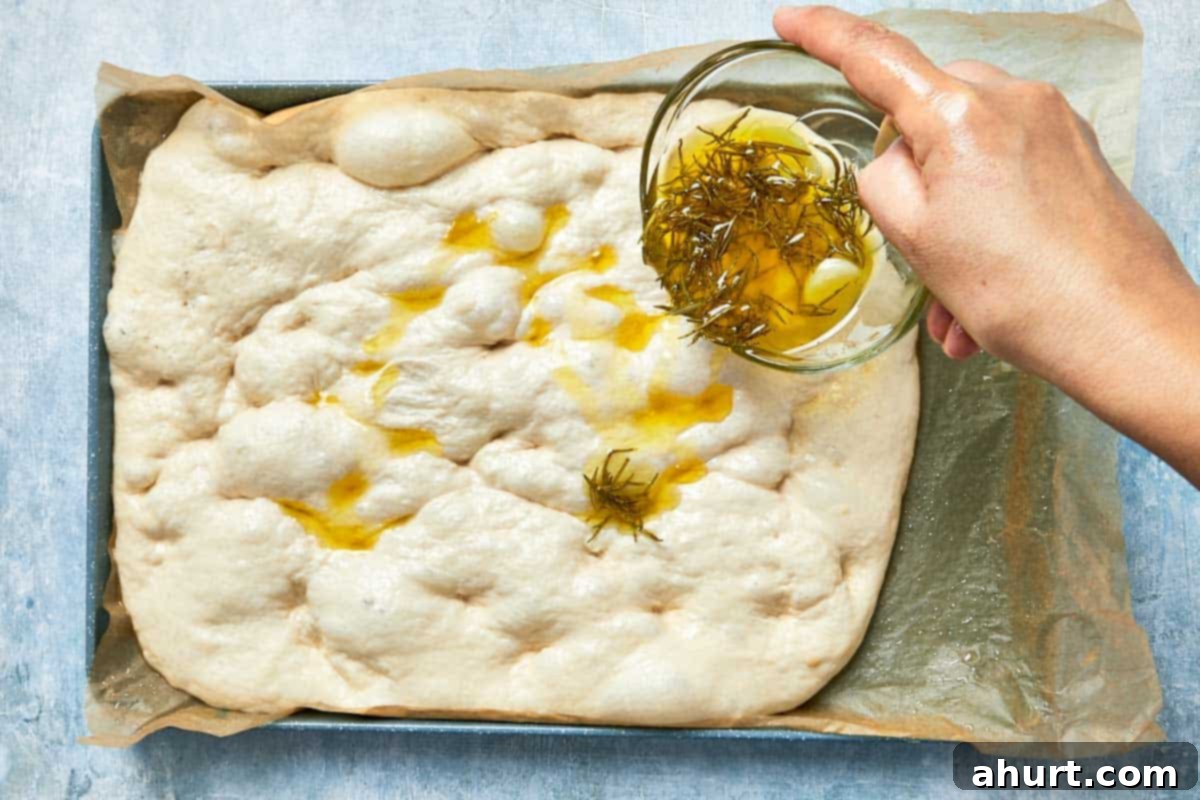 Effortless Homemade Focaccia 16 Infused oil being drizzled over dimpled dough before baking, ready for the oven.
