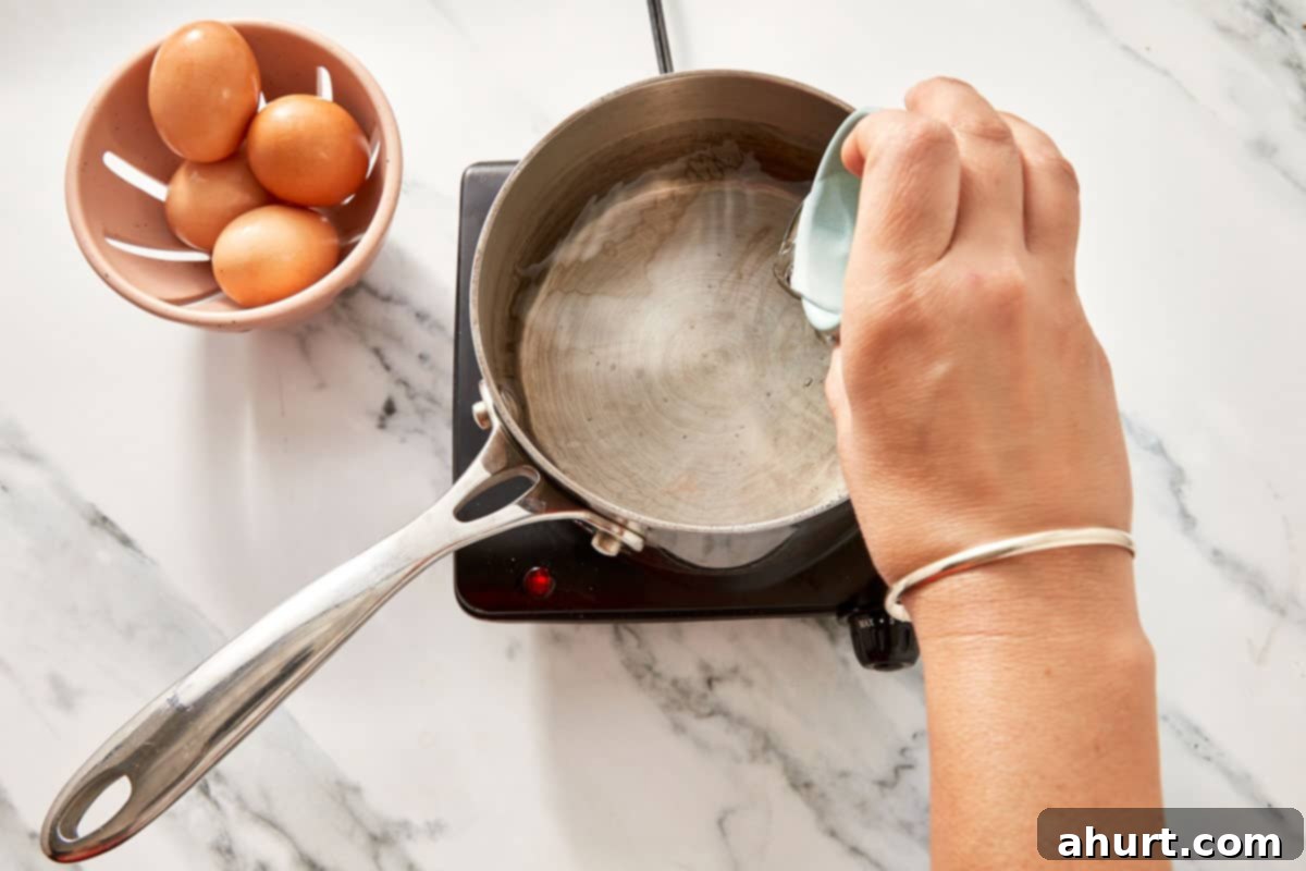 Mastering Perfect Poached Eggs 4 A hand holding a ramekin over a saucepan with gently simmering water and a spoon creating a whirlpool.
