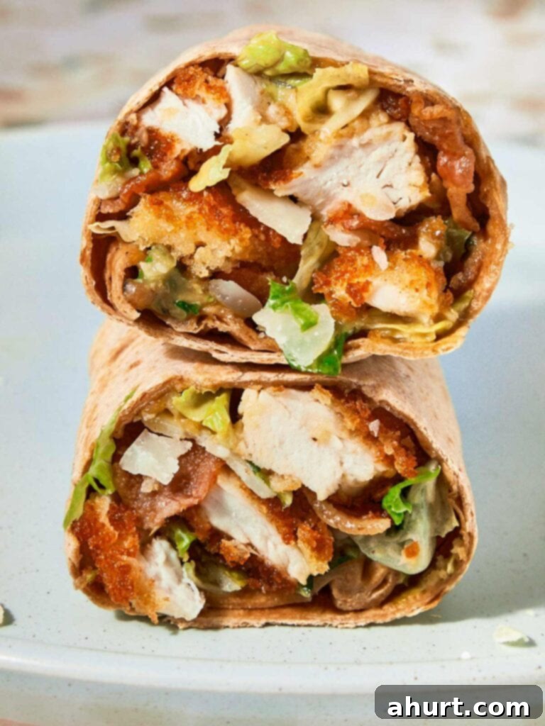 Signature Crispy Caesar Wrap 2 A perfectly toasted Crispy Chicken Caesar Wrap, cut in half to show the delicious filling, held in a hand.