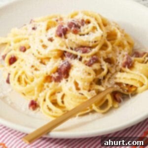 Velvet Carbonara Bliss 11 A plate of finished pasta carbonara on a red-striped napkin, topped with crispy pancetta and extra cheese.