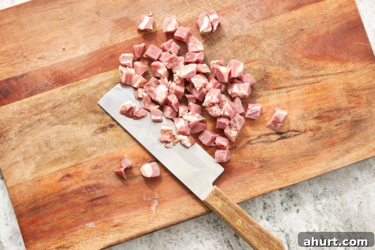 Velvet Carbonara Bliss 4 Raw pancetta cut into small cubes on a wooden cutting board, ready to be crisped.