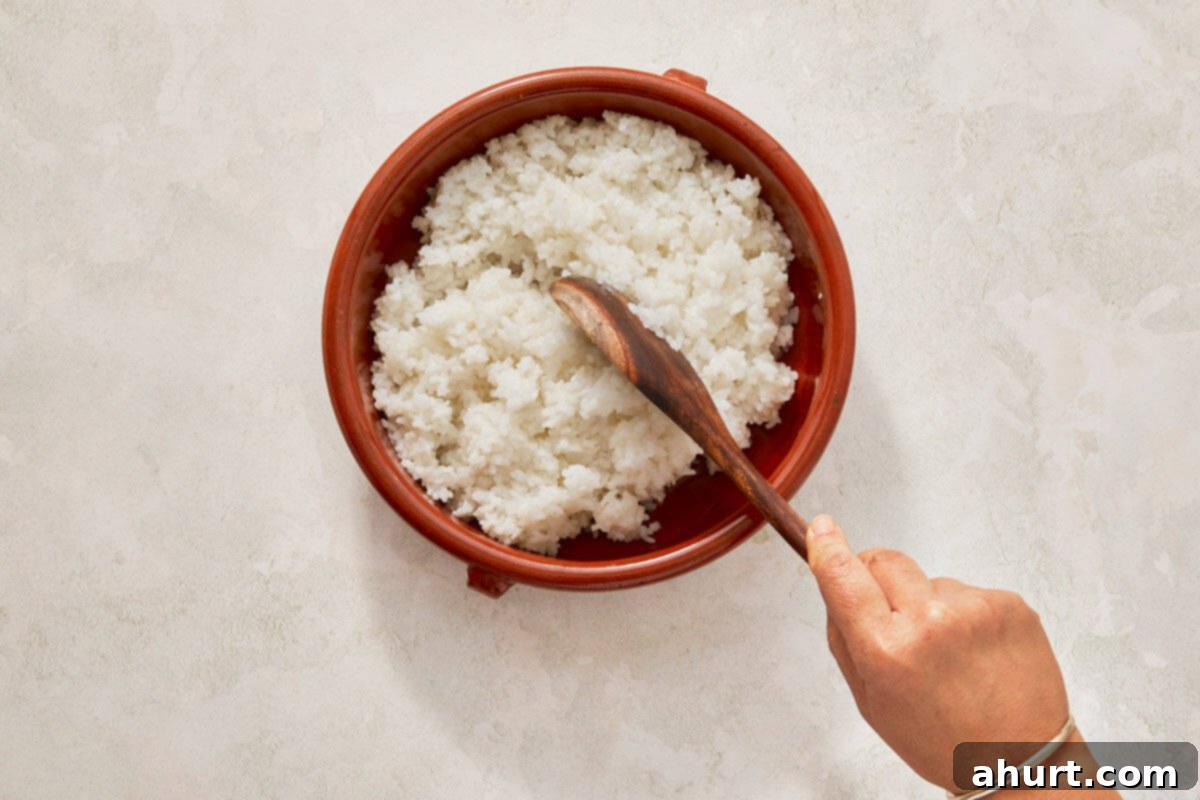 Easy At-Home Sushi Bake 5 Hand grips a wooden spoon, poised over a bowl of rice