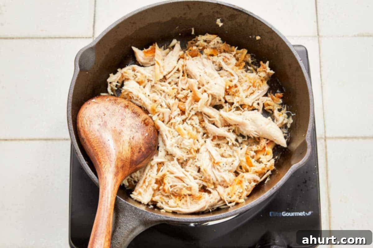 Green Enchiladas 4 A skillet with sautéed shredded chicken and a wooden spoon.