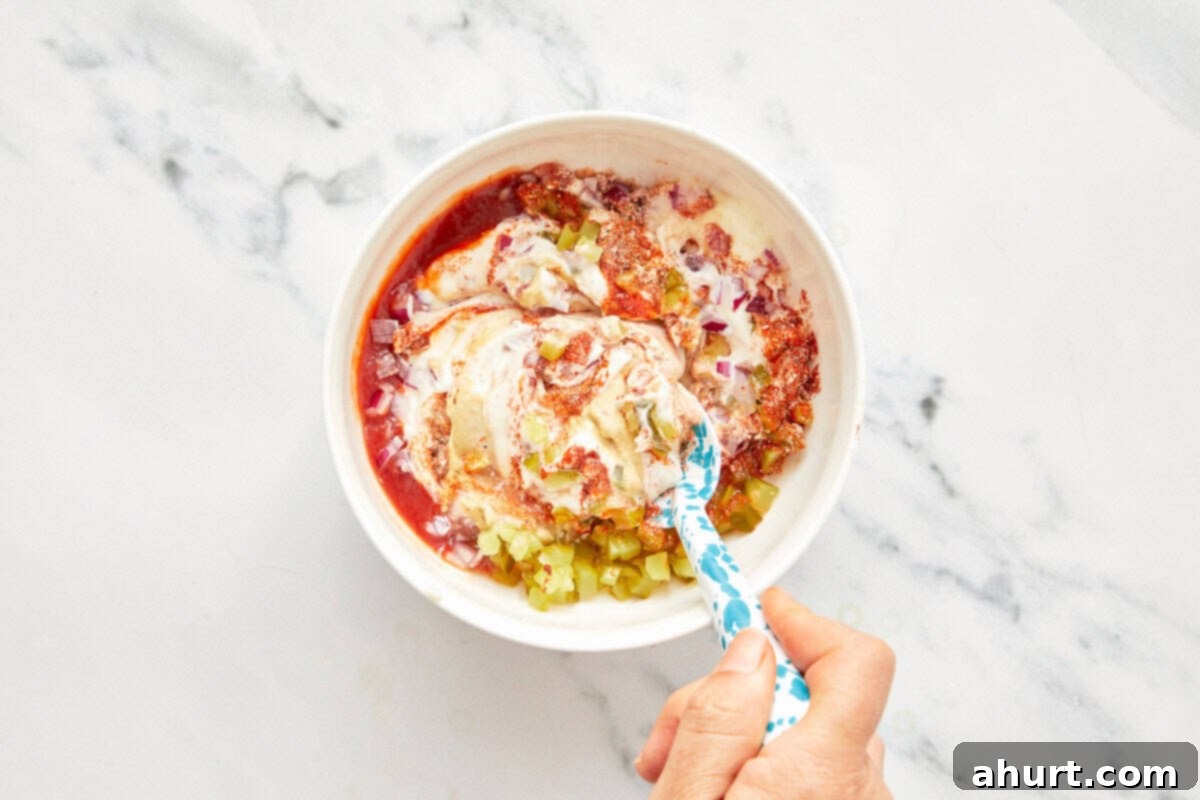 Smash Burger Taco Mashup 4 Bowl with mayonnaise, ketchup, chopped pickles, diced red onion, and spices being mixed with a spoon for burger sauce.