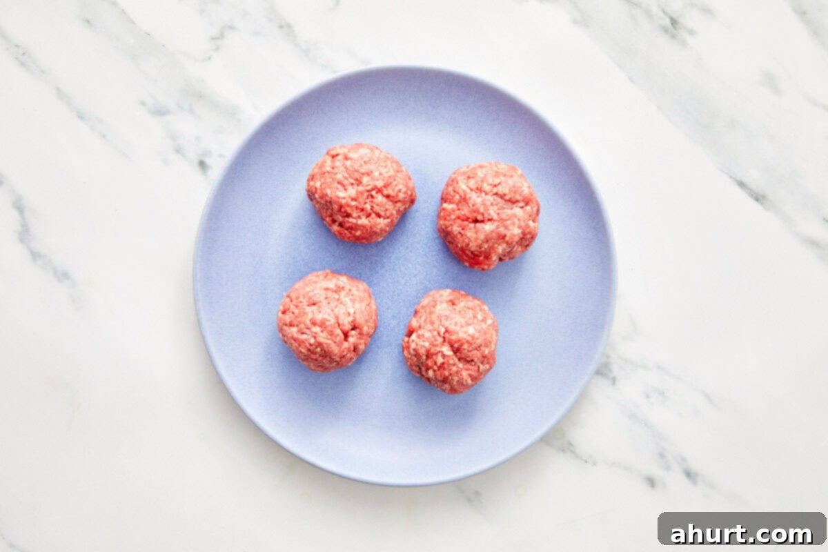 Smash Burger Taco Mashup 5 Four raw ground beef balls on a light blue plate, seasoned and ready for smashing into burger tacos.