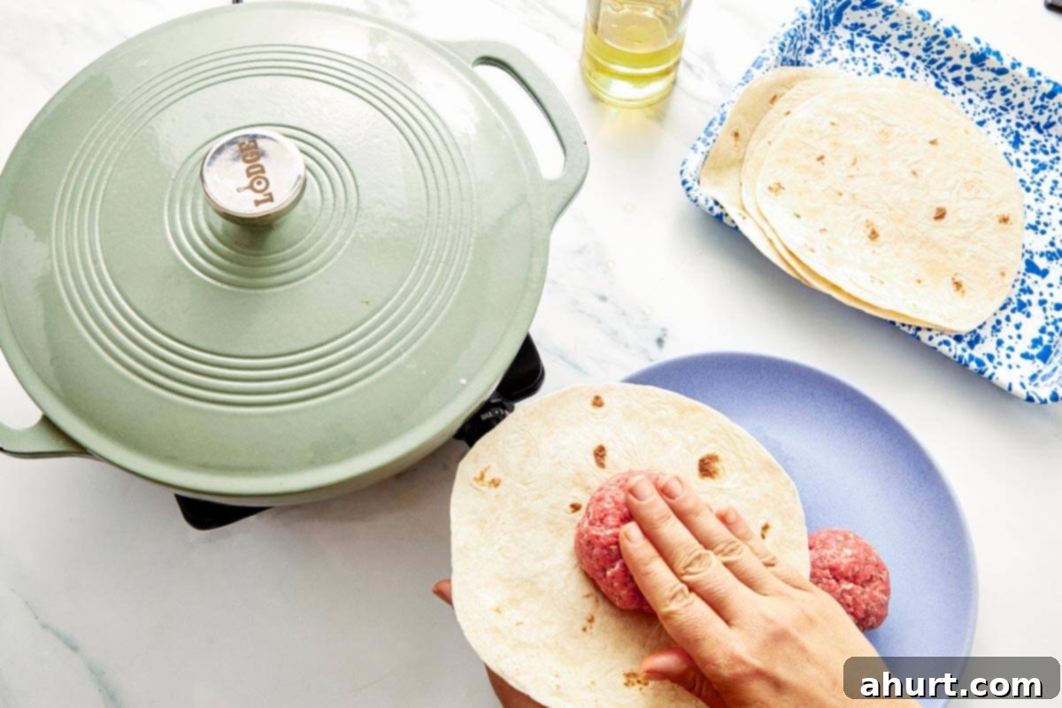 Smash Burger Taco Mashup 6 Pressing a raw beef ball onto a flour tortilla before cooking in a skillet to prepare for smashing.
