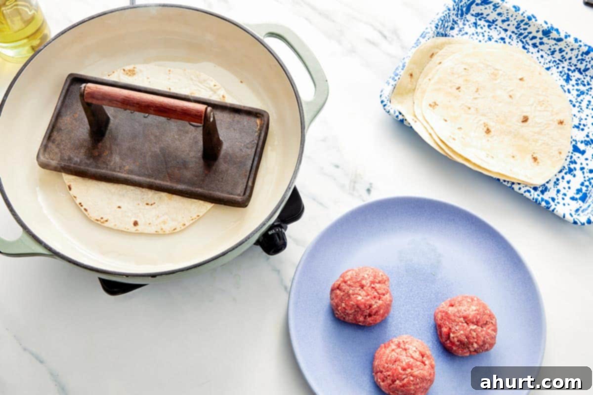 Smash Burger Taco Mashup 7 Tortilla with beef being pressed down in a skillet using a metal grill press for maximum crispness.
