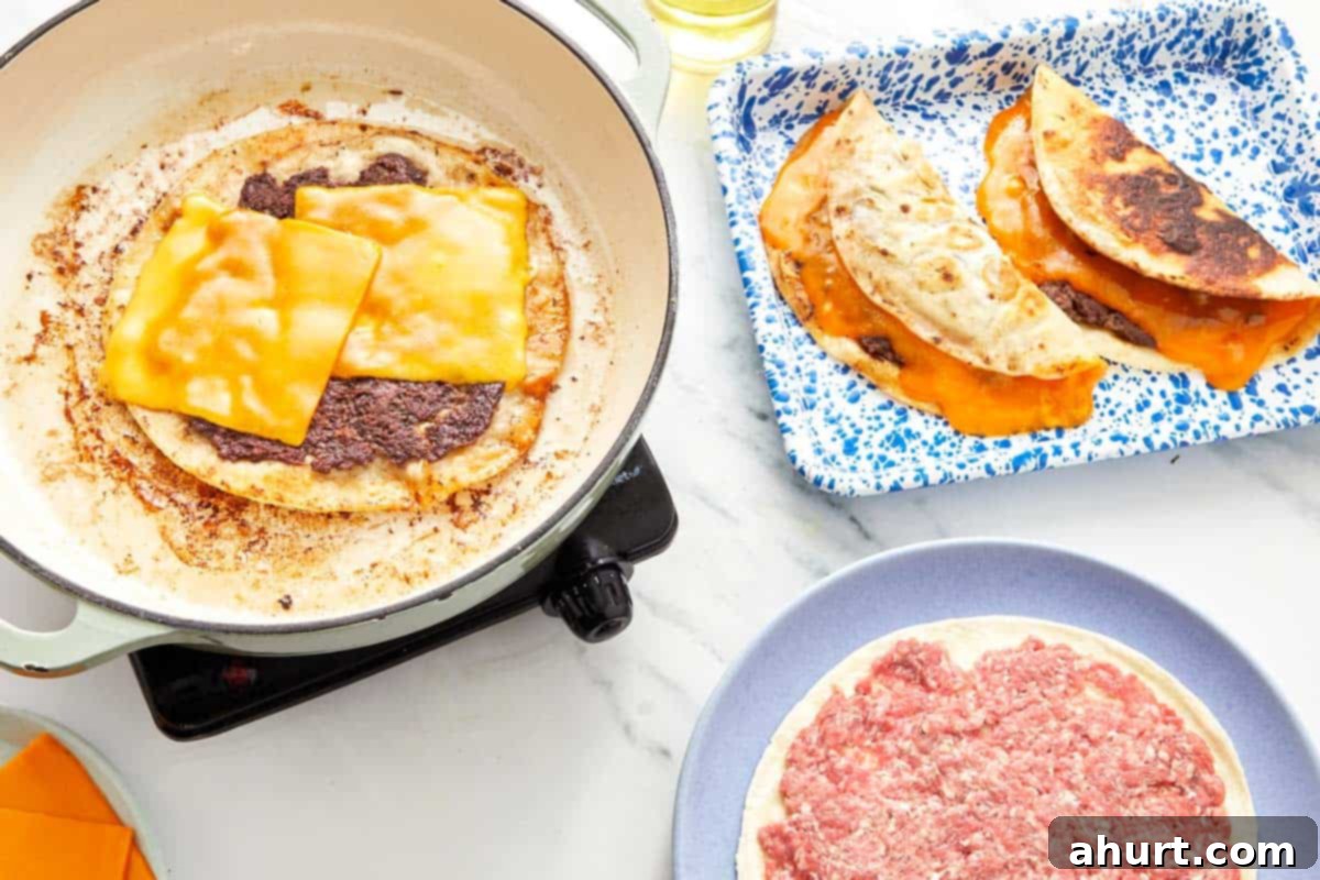Smash Burger Taco Mashup 8 Cooking beef-topped tortillas with melted cheddar cheese in a skillet, with finished cheesy tacos on the side.