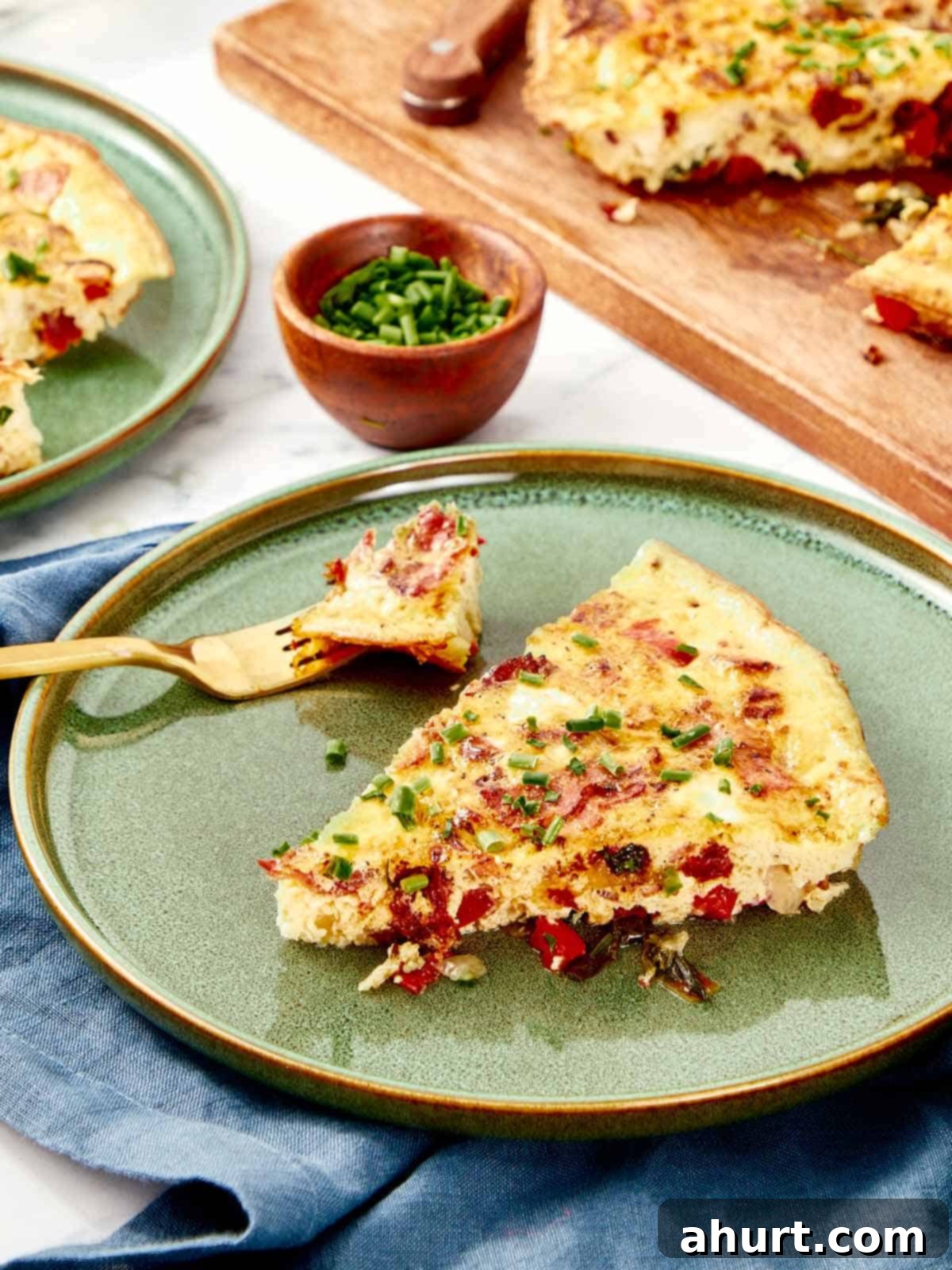 Frittata The Brunch Showstopper 10 A perfectly portioned slice of golden frittata, showcasing the layers of bacon, feta, and vegetables, served on an elegant green ceramic plate and garnished with fresh, finely chopped chives, ready to be eaten with a fork.