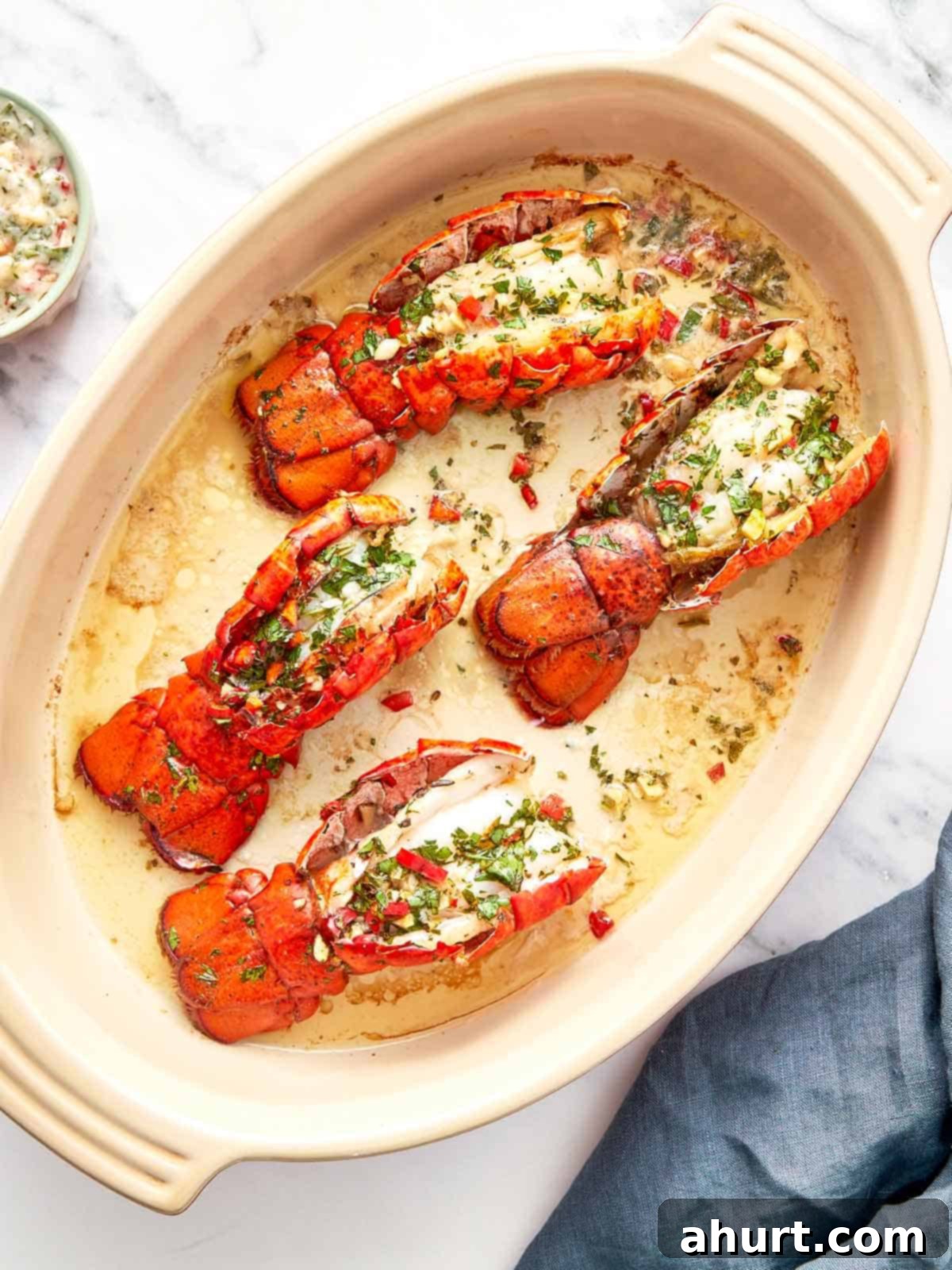 Sizzling Lobster Tails with Herbaceous Chimichurri 10 Four broiled lobster tails in a baking dish, topped with chimichurri butter and garnished with fresh herbs and red chili.