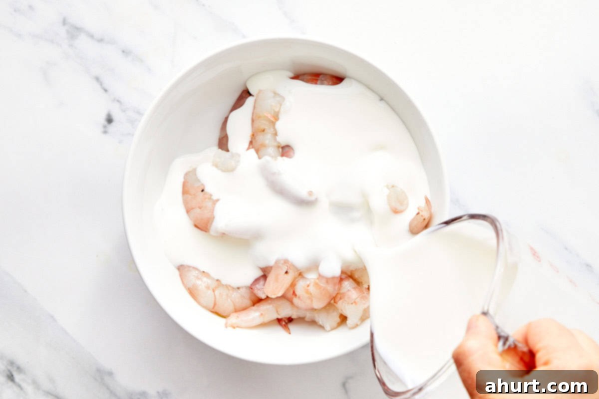 Dynamite Shrimp 4 Raw jumbo shrimp marinating in a white bowl with buttermilk, demonstrating the first step of the Bang Bang Shrimp recipe.