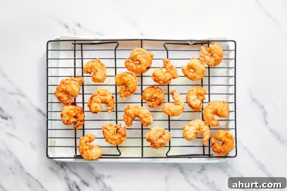 Dynamite Shrimp 8 Freshly fried Bang Bang Shrimp draining excess oil on a wire rack over paper towels, ensuring maximum crispness.