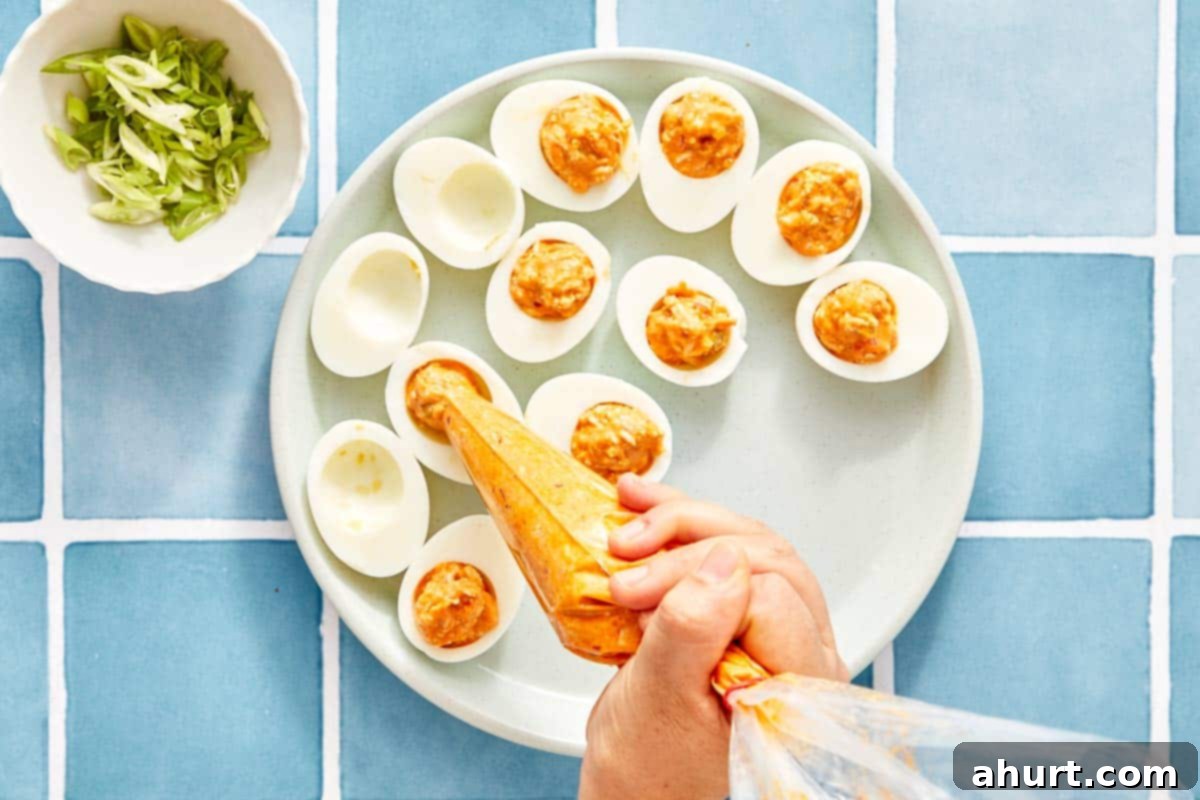 Spicy Buffalo Chicken Deviled Eggs 6 Piping the filling into egg whites on a platter.