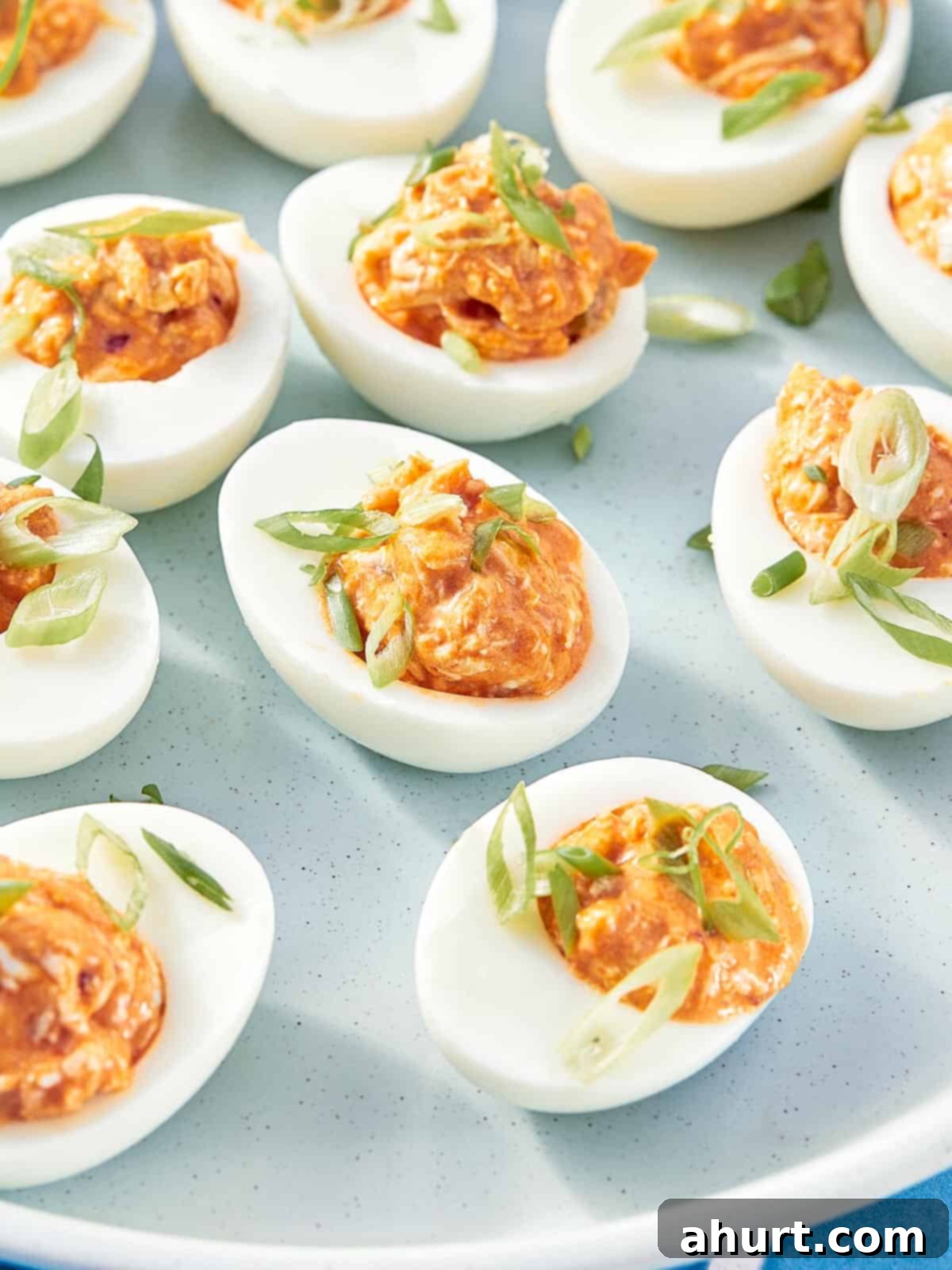 Spicy Buffalo Chicken Deviled Eggs 8 Buffalo chicken deviled eggs topped with green onion on a plate.