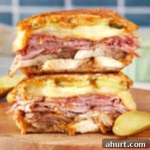 The Iconic Pressed Cuban 11 Stacked Cuban sandwich with layers of roast pork, ham, salami, Swiss cheese, pickles, and mustard, pressed until golden and melty.