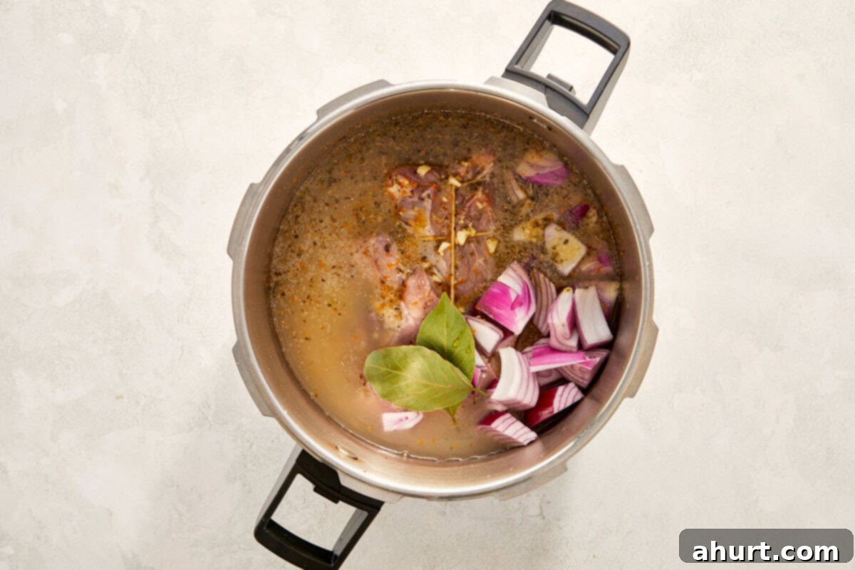 The Iconic Pressed Cuban 4 Pork shoulder marinating with onions and bay leaves in a pot, ready for slow cooking to absorb rich flavors.
