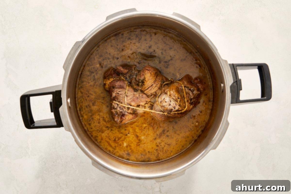 The Iconic Pressed Cuban 5 Cooked, tender pork in rich broth inside a pressure cooker, ready to be sliced and sauced for Cuban sandwiches.
