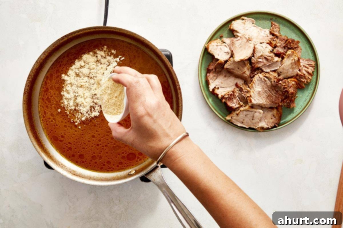 The Iconic Pressed Cuban 6 A hand adding cornflour to a simmering sauce in a pan, thickening the rich pork cooking liquid for the Cuban sandwich.