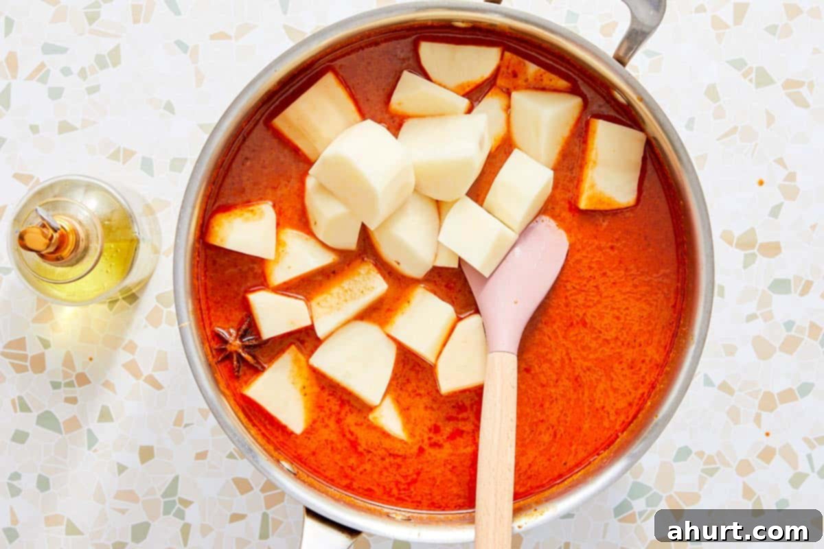 Rich Massaman Beef Curry 7 Cubed potatoes added to a pot of simmering Massaman curry sauce.