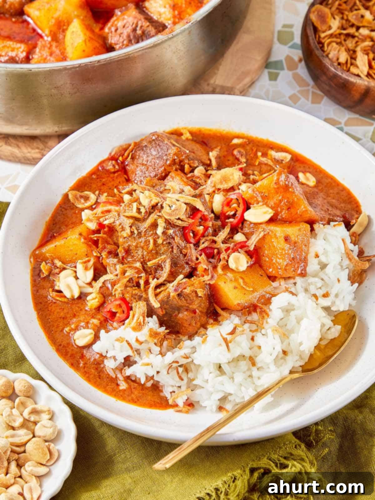 Rich Massaman Beef Curry 10 Close-up of a plate of Massaman Beef Curry with tender beef, soft potatoes, and rich sauce, garnished with peanuts, red chili, and crispy shallots, served with jasmine rice.